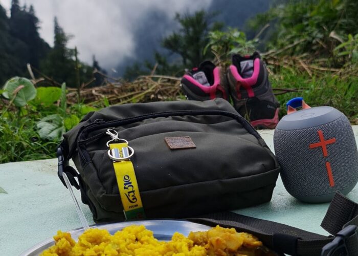 Kareri lake trek - A beautifully captured moment from the Kareri Lake trek, featuring a trekking bag, speaker, shoes, and a plate of food with a misty mountain backdrop.