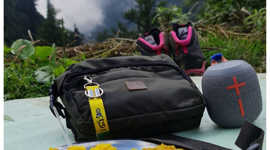 Kareri lake trek - A beautifully captured moment from the Kareri Lake trek, featuring a trekking bag, speaker, shoes, and a plate of food with a misty mountain backdrop.